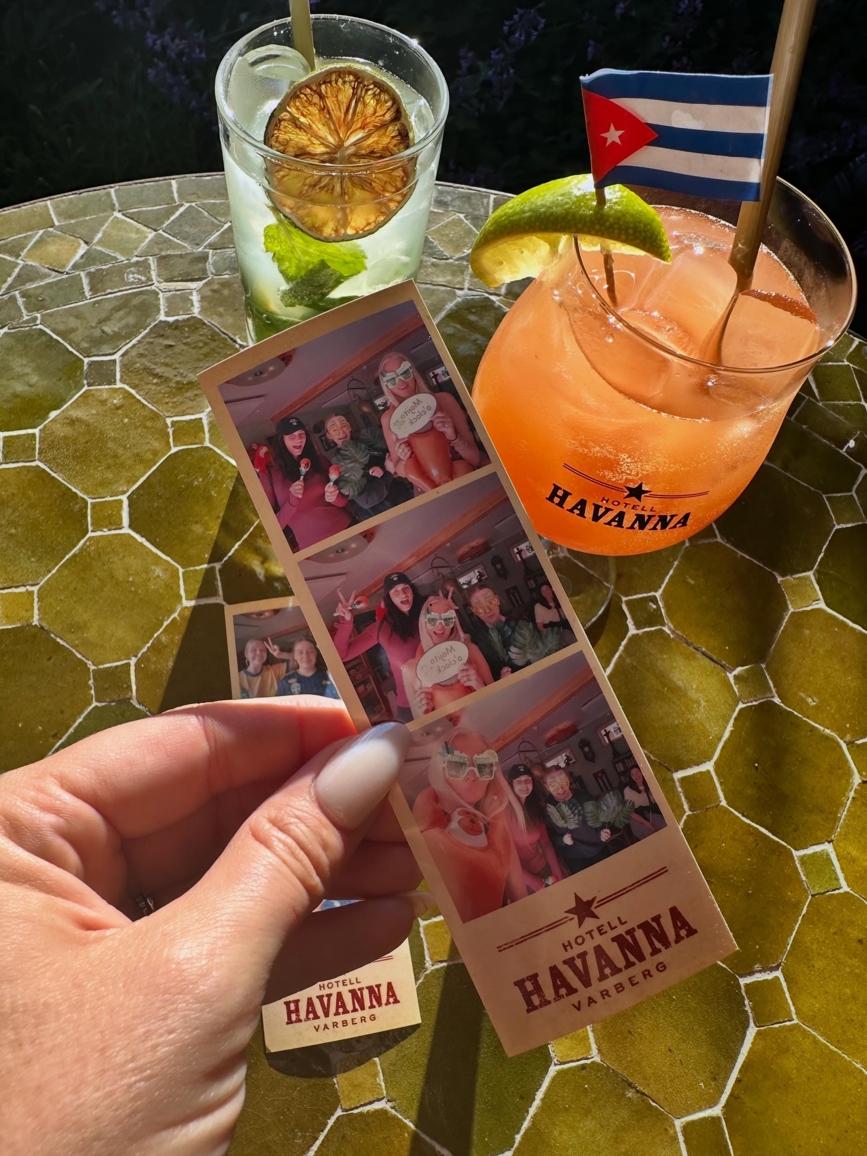 Hand som håller en nyutskriven fotoremsa från Mabooth bredvid cocktails